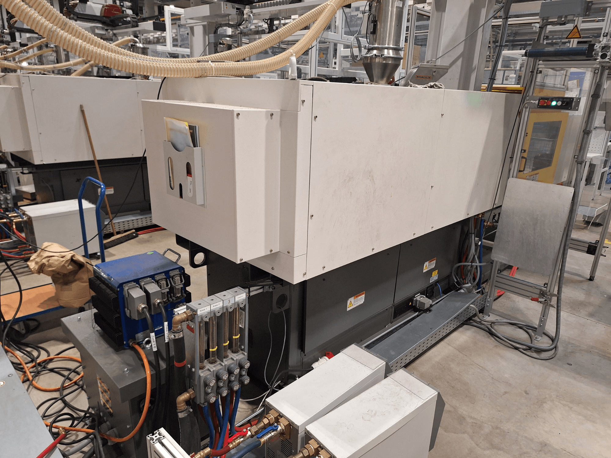 Промышленное оборудование на заводе; большой станок с панелью управления, шлангами и электрическими соединениями, вид сбоку.