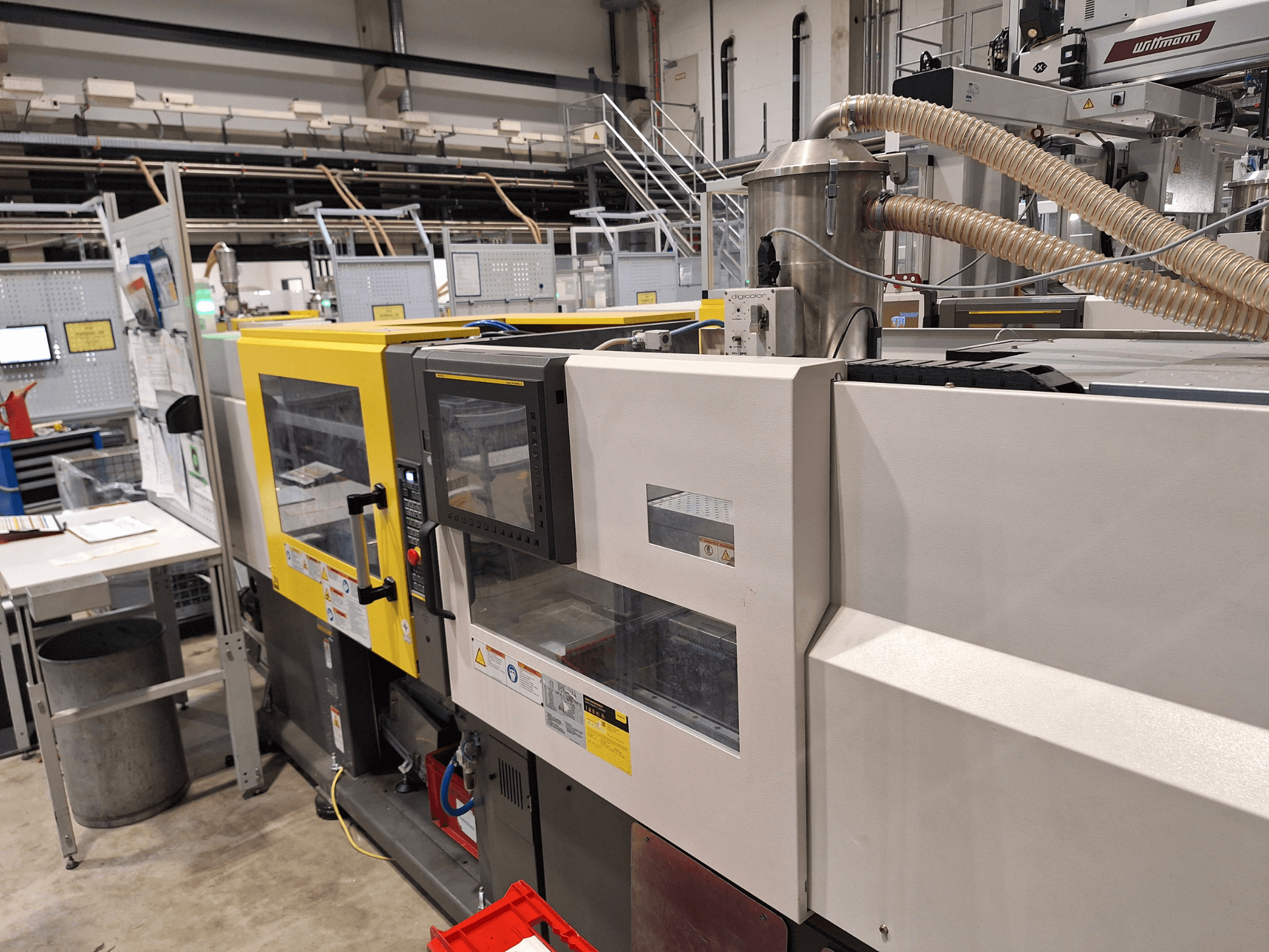 Вид спереди на многоцветный термопластавтомат с желтыми и серыми секциями, с панелью управления и выхлопной системой.