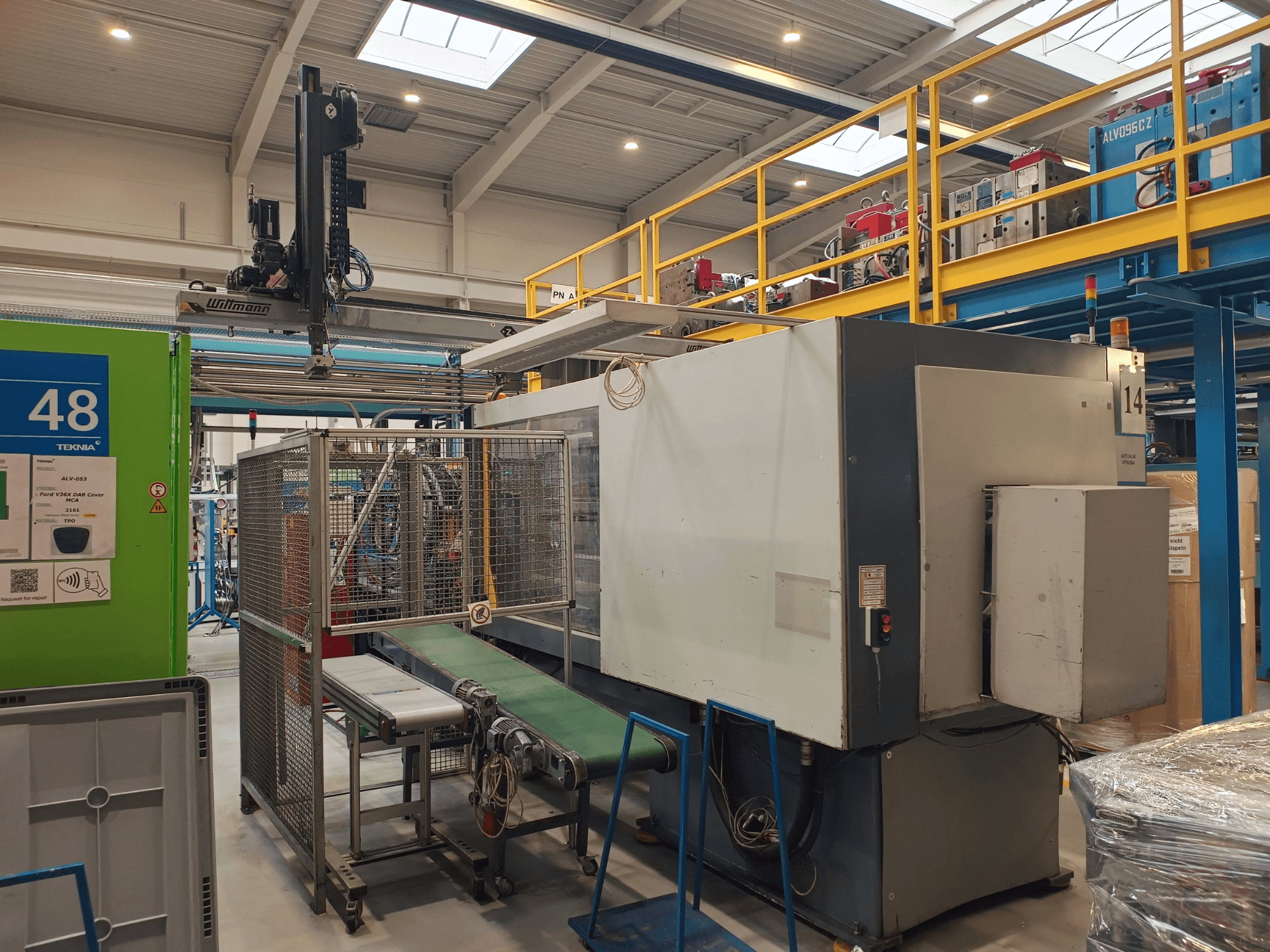 Оборудование для автоматизации производства с зеленым конвейером с надписью "48" и мостовым краном; вид сбоку на станок на полу завода.